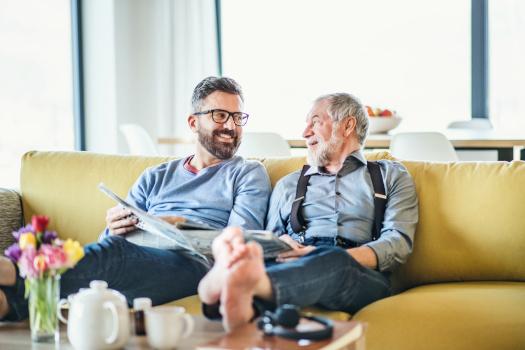 An adult child sitting with an elderly parent, speaking warmly and with care